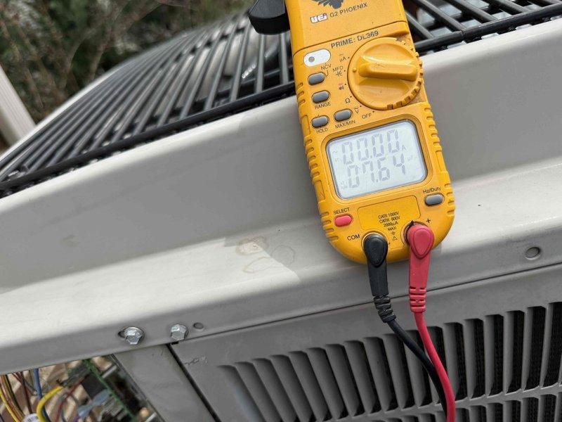 Completed comprehensive Gold AC inspection on 15-year-old single-unit system with air handler located in basement. Performed full system diagnostics including electrical testing with digital multimeter, verified refrigerant line connections at outdoor condenser unit, inspected condenser coil fins and exterior housing for proper operation, and confirmed system is functioning correctly with all components operating within normal parameters. Unit exterior and surrounding area show normal wear consistent with age, with minor vegetation growth in mulch bed noted around condenser pad.