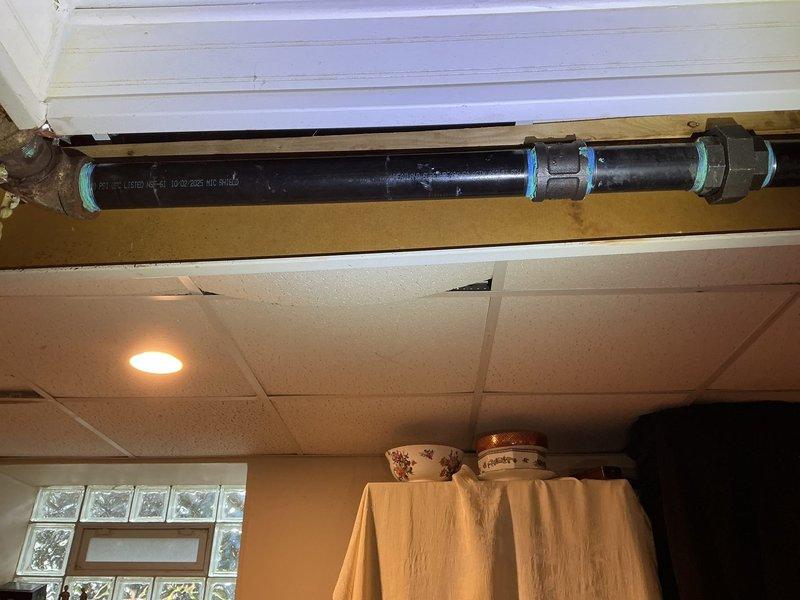 Accessed plumbing infrastructure through wall and ceiling openings to repair and replace damaged piping sections. Installed new black plastic pipe with compression fittings to address leak in horizontal supply line running above kitchen ceiling. Replaced corroded copper piping that exhibited green patina deterioration with modern plastic piping system, ensuring proper connections and secure mounting to structural framing members.