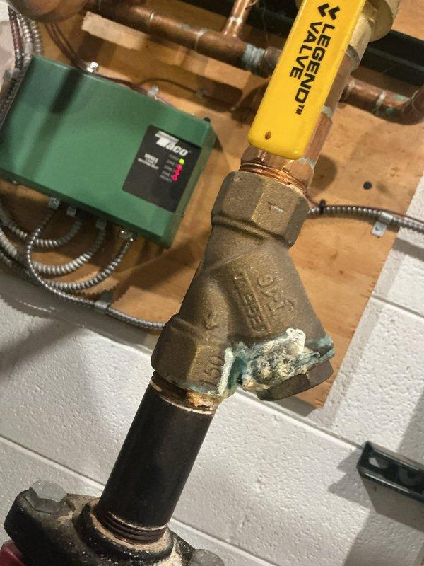 Responded to service call for boiler system displaying blockage error and not operating properly. Upon arrival, performed diagnostic inspection of 10+ year old boiler system located in basement. Examined Grundfos circulation pump and associated control components, noting operational status of Taco zone control panel with multiple indicator lights. Inspected copper piping connections and Legend valve assembly, observing turquoise-green corrosion and mineral deposits on brass valve body indicating copper oxidation. Assessed system for potential blockages in circulation system and verified proper pump operation. Documented equipment condition through photographs showing circulation pump, control panel status, and valve assembly with visible corrosion buildup. Diagnostic evaluation completed to determine cause of blockage error and system malfunction.