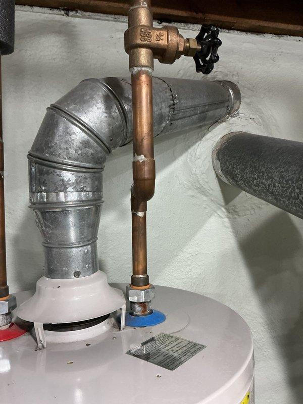 Responded to service call for residential tanked water heater with reported leak and water spray. Upon arrival, performed visual inspection of unit and associated plumbing connections. Examined copper supply lines, brass fittings, pressure relief valve assembly, and galvanized vent piping for signs of active leakage or water damage. Inspected T-junction fittings, shut-off valves, and threaded connections at top of water heater tank for moisture, corrosion, or compromised seals. Assessed condition of pipe insulation and verified proper installation of temperature and pressure relief valve. Documented existing plumbing configuration including copper and galvanized piping connections, valve positioning, and overall system condition through photographic evidence for service records.