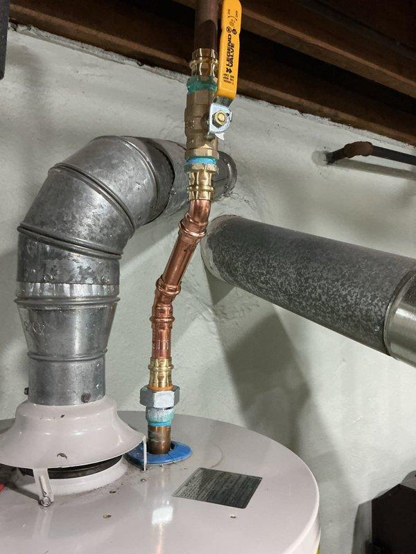 Responded to service call for residential tanked water heater with reported leak and water spray. Upon arrival, performed visual inspection of unit and associated plumbing connections. Examined copper supply lines, brass fittings, pressure relief valve assembly, and galvanized vent piping for signs of active leakage or water damage. Inspected T-junction fittings, shut-off valves, and threaded connections at top of water heater tank for moisture, corrosion, or compromised seals. Assessed condition of pipe insulation and verified proper installation of temperature and pressure relief valve. Documented existing plumbing configuration including copper and galvanized piping connections, valve positioning, and overall system condition through photographic evidence for service records.