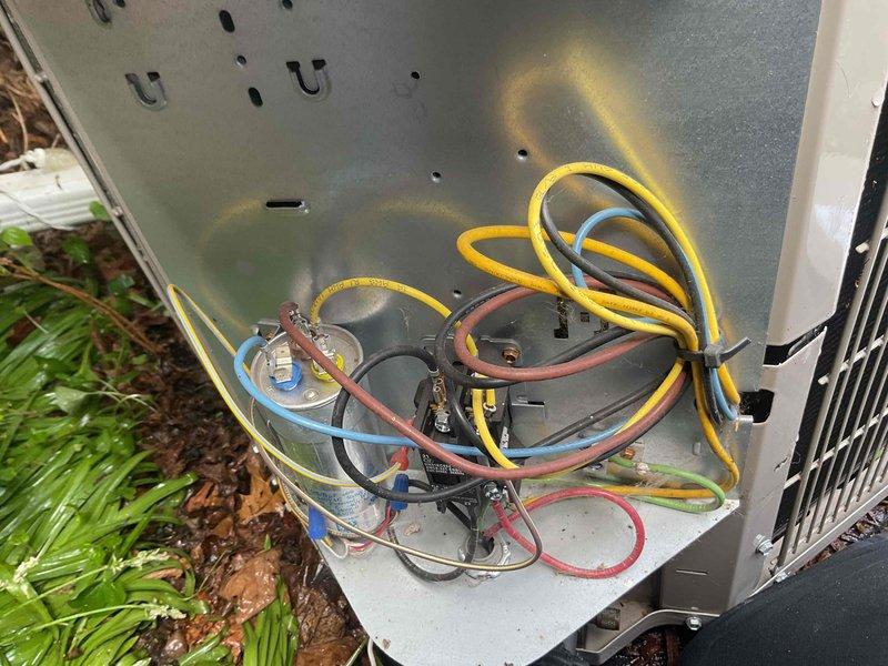 Completed comprehensive Gold AC inspection on 4-year-old air conditioning system. Performed full tune-up service including inspection of outdoor condenser unit, electrical connections, capacitor, and contactor assembly. Verified all wiring connections were secure, checked refrigerant levels, cleaned condenser coils, and tested system operation. All electrical components including capacitor and contactors were found to be in proper working condition. System operating within manufacturer specifications with no deficiencies noted. Unit located in basement with outdoor condenser positioned against exterior brick wall. Documentation photos captured of electrical compartment and exterior condenser unit for service records.