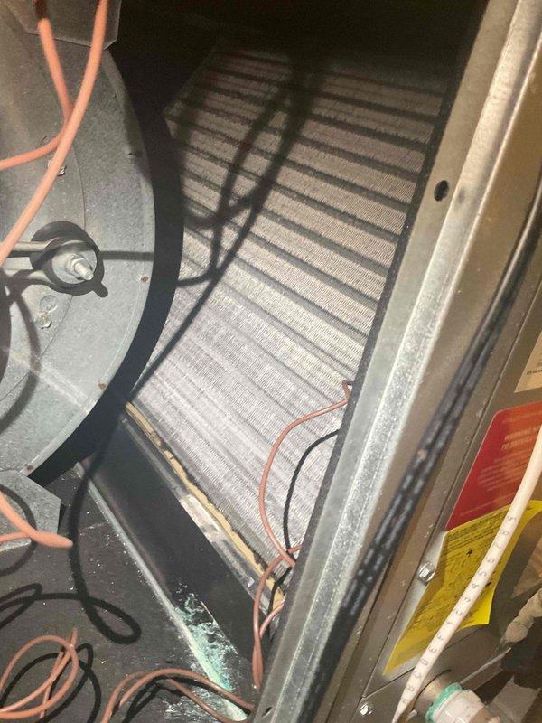 Completed annual Gold AC inspection on 5-year-old air conditioning system located in attic. Performed comprehensive tune-up including visual inspection of evaporator coil assembly, which revealed ice and frost buildup along the bottom edge of the coil and drainage pan area. This condition indicates potential airflow restriction, refrigerant charge issues, or drainage problems requiring further diagnosis. Inspected blower compartment and motor assembly, noting loose electrical wiring arrangement within the housing. Documented all findings with photographs for service records. System requires follow-up to address freezing condition and ensure proper operation during cooling season.