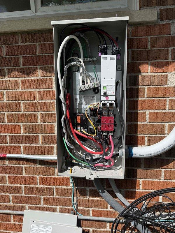 Inspected and documented Generac automatic transfer switch installation and electrical panel configuration. Replacement part has been ordered and is currently being held at the shop pending installation. System components photographed for warranty documentation, including 200A transfer switch, control module, and associated electrical connections within exterior-mounted enclosure.