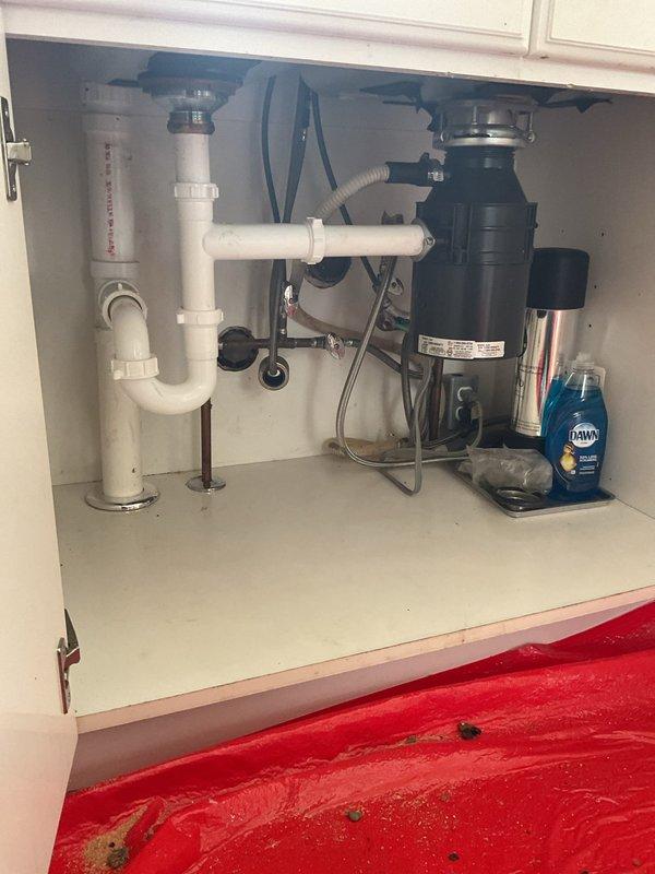 Completed stack replacement in residential property, removing and replacing the main vertical drain pipe running from the kitchen level down through the basement. Accessed under-sink plumbing connections at kitchen cabinet, disconnecting existing PVC drain lines and garbage disposal tie-ins from the old stack. Removed deteriorated vertical drainage pipe section and installed new white PVC stack with proper fittings and connections. Reconnected kitchen sink drain assembly including trap configuration and garbage disposal discharge line to new stack. Secured all pipe joints with appropriate primer and cement, ensuring watertight seals throughout the system. Tested drainage flow from kitchen fixtures to verify proper function and confirmed no leaks at connection points in both the cabinet area and basement termination.