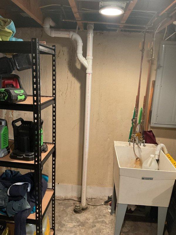Completed stack replacement in residential property, removing and replacing the main vertical drain pipe running from the kitchen level down through the basement. Accessed under-sink plumbing connections at kitchen cabinet, disconnecting existing PVC drain lines and garbage disposal tie-ins from the old stack. Removed deteriorated vertical drainage pipe section and installed new white PVC stack with proper fittings and connections. Reconnected kitchen sink drain assembly including trap configuration and garbage disposal discharge line to new stack. Secured all pipe joints with appropriate primer and cement, ensuring watertight seals throughout the system. Tested drainage flow from kitchen fixtures to verify proper function and confirmed no leaks at connection points in both the cabinet area and basement termination.