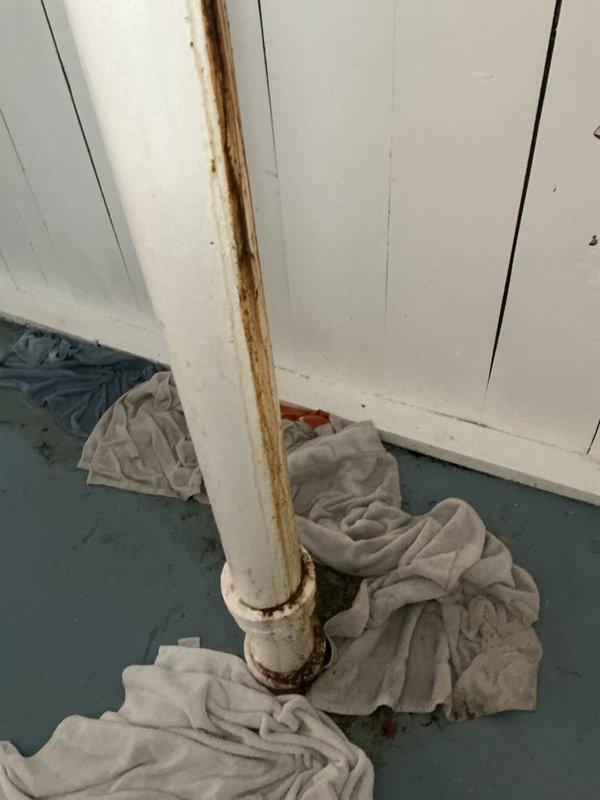 # Emergency Plumbing Repair - Basement Pipe Leak

Responded to an active water leak in the basement caused by a cracked vertical PVC drain pipe. Upon arrival, discovered a significant vertical split running along the length of the pipe with heavy rust-colored staining indicating ongoing water seepage. Temporary measures were implemented by placing absorbent towels at the base of the pipe to contain water damage to the basement floor area.

Documented the extent of the damage through photographic evidence, capturing the crack location at the coupling joint and the rust discoloration pattern. The pipe showed signs of deterioration with metal corrosion visible within the PVC system, suggesting contamination or internal component failure. The leak was confined to the basement utility area with no indication of spread to upper floors at the time of service.

Assessed the vertical pipe running from floor to ceiling and identified the compromised section requiring replacement. The rust staini
