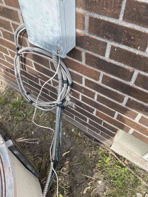 Provided comprehensive estimate for complete air conditioning system replacement of 25-year-old outdoor unit that ceased operation last year. Unit located on side of house shows significant weathering, age-related deterioration, and discoloration on exterior surfaces. Assessed existing installation including copper refrigerant lines, electrical disconnect box, mounting pad condition, and associated electrical conduit system for replacement planning considerations.