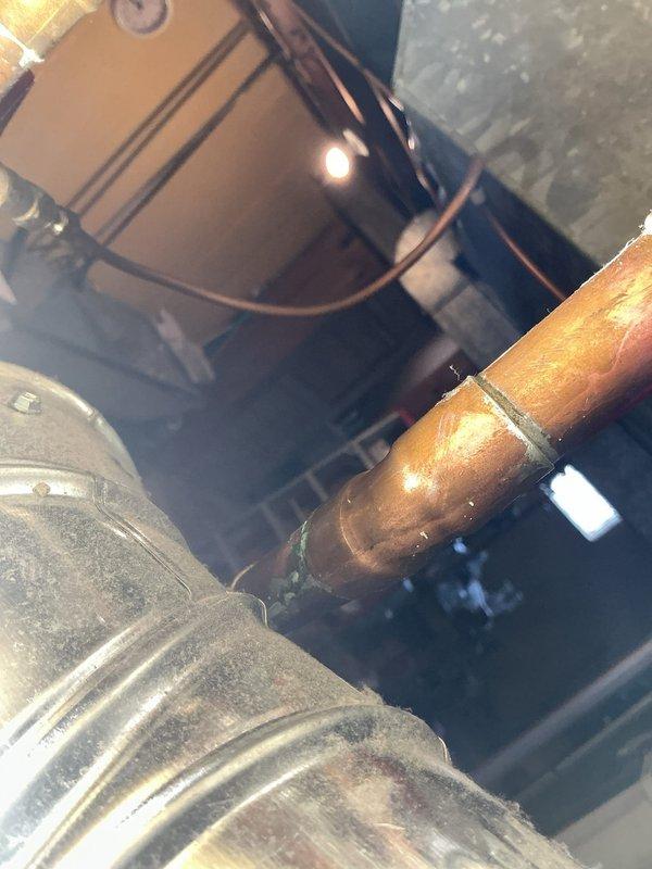 Responded to service call for reported leak on hot water line at water heater installed November 2021 under active warranty. Upon arrival, performed thorough diagnostic inspection of water heater and associated copper piping connections. Examined top-mounted heat trap assembly, hot water outlet connections, and all visible copper pipe joints for signs of active leakage or moisture accumulation. Inspected flexible duct connector and surrounding mechanical components in utility area. Verified integrity of pipe fittings, including white plastic clamps and galvanized metal connections at tank crown. Assessed condition of all accessible plumbing connections and determined source of reported leak for appropriate corrective action.