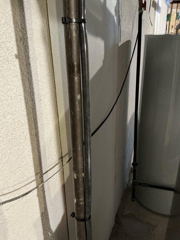 Completed comprehensive Gold AC inspection on 19-year-old residential air conditioning system with air handler located in basement. Performed thorough evaluation of all system components, including visual inspection of refrigerant lines, electrical connections, and condensate drainage. Verified proper system operation and documented equipment condition with photographic records of the installation area showing piping, electrical wiring, and cabinet configuration.