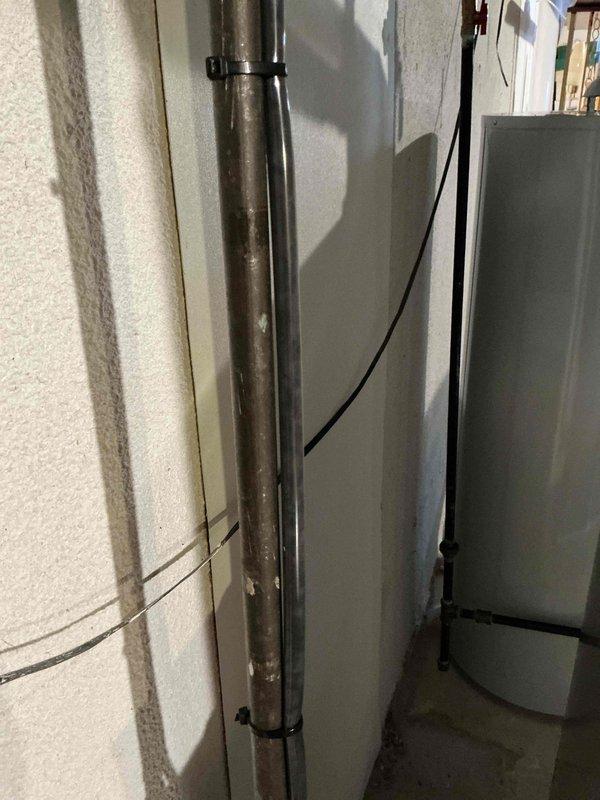 Completed comprehensive Gold AC inspection on 19-year-old residential air conditioning system with air handler located in basement. Performed thorough evaluation of all system components, including visual inspection of refrigerant lines, electrical connections, and condensate drainage. Verified proper system operation and documented equipment condition with photographic records of the installation area showing piping, electrical wiring, and cabinet configuration.