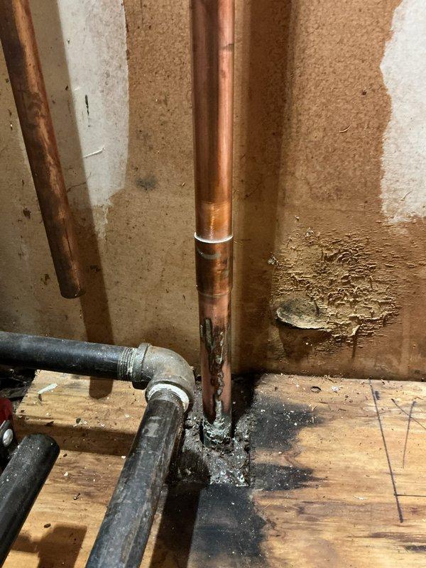 Responded to service call for leaking hot water supply line on commercial water heater serving six apartment units located in mechanical room. Upon arrival, inspected copper supply piping and identified active leak at corroded connection point near base of vertical supply line. Copper piping exhibited significant oxidation, green patina buildup, and corrosion damage consistent with long-term moisture exposure and age-related deterioration. Wall surfaces and flooring around piping showed evidence of water damage and staining from ongoing leak. Shut down water supply to affected heater to prevent further water damage. Assessed extent of corrosion on vertical copper runs and determined compromised pipe sections required replacement to restore system integrity. Documented existing conditions including corroded pipe sections, deteriorated fittings, and water-damaged surrounding areas for repair recommendations. Provided assessment that hot water supply piping system requires replacement of 