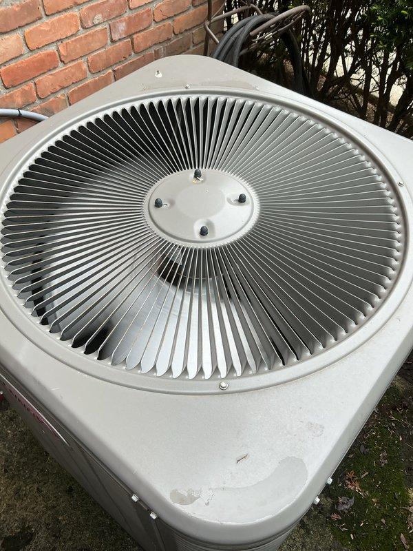Completed comprehensive Gold AC inspection on single residential split system with basement air handler and outdoor condenser unit, less than 10 years old. Performed visual assessment of outdoor condenser positioned on concrete pad against brick wall, confirming proper clearance and mounting. Inspected fan assembly through top grille, noting clean radial fins and well-maintained condition. Verified refrigerant lines and electrical connections at exterior unit, observing proper routing of gray flexible conduit along brick wall. Documented unit showing normal outdoor weathering with functional components and no visible damage. System confirmed operational at time of inspection with homeowner present.