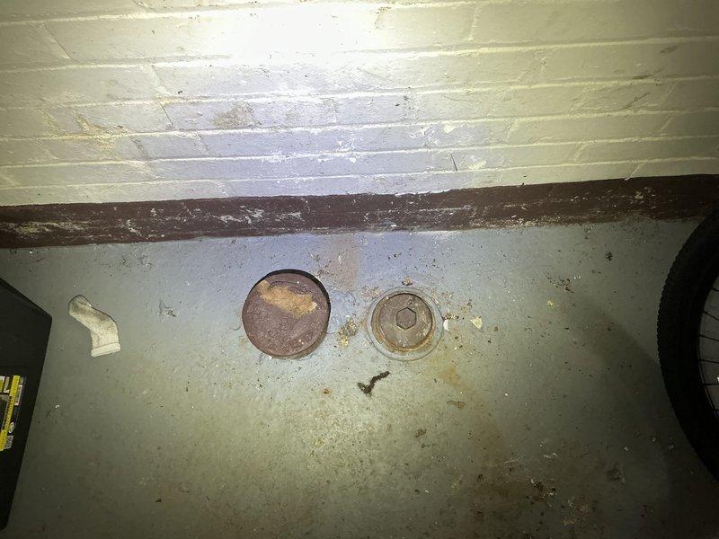 # Main Drain Cleanout Service

Responded to a whole-house drainage issue in an 85-year-old residential property with the problem originating in the basement house trap. Upon inspection, located the deteriorated house trap assembly in the basement floor, which was causing drainage problems throughout the entire plumbing system. The existing trap showed significant age-related corrosion and structural compromise consistent with original installation from approximately 80-90 years ago.

Assessed the condition of the cast iron house trap and surrounding cleanout access points embedded in the concrete basement floor. Documented the existing configuration, including the corroded circular access cover and hex-style cleanout cap, both showing extensive deterioration around the edges and mounting points. The trap's compromised condition was affecting all fixtures and drains in the residence.

Provided comprehensive evaluation of the house trap replacement requirements, including access consider
