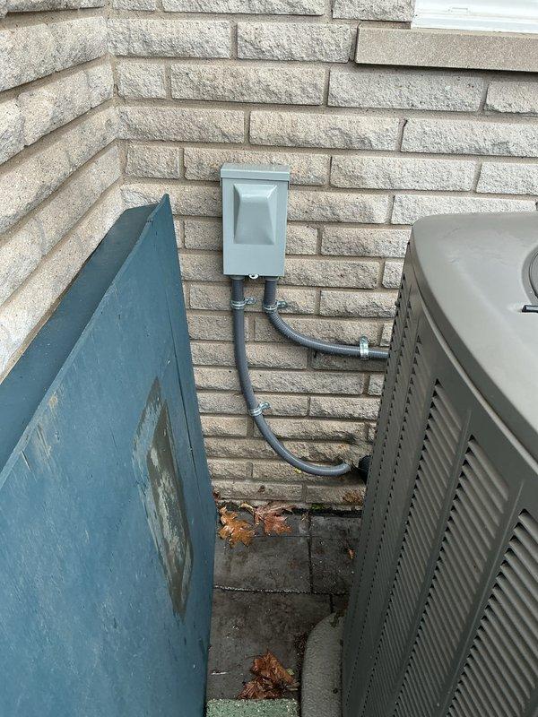 Completed comprehensive Gold AC Inspection on outdoor air conditioning unit located on exterior patio. Performed full system tune-up including inspection of electrical disconnect box, conduit connections, and unit housing. Verified proper operation of all components, checked electrical connections at disconnect panel, and documented equipment condition with photographic records showing disconnect box in open position with visible specifications panel and PVC conduit routing along exterior wall. Unit appears to be in functional condition with all exterior components properly secured and maintained.