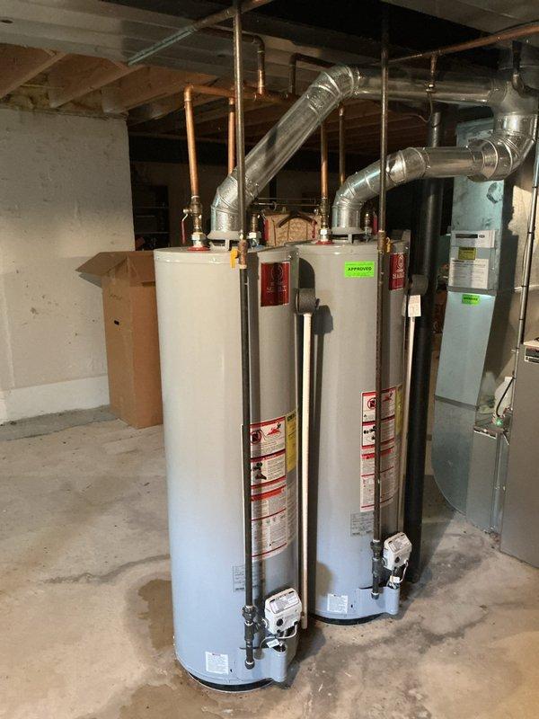 Responded to service call for leaking 40-gallon water heater, approximately 11 years old, located in basement. Upon inspection, confirmed active leak on aging unit and assessed dual water heater system with backflow preventer assembly mounted on exterior brick wall. Documented current condition of both water heaters, associated copper piping, vent connections, and corroded backflow prevention device with deteriorating valve components. Provided comprehensive replacement quote for failed water heater unit.