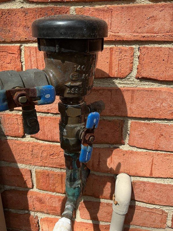 Responded to service call for leaking 40-gallon water heater, approximately 11 years old, located in basement. Upon inspection, confirmed active leak on aging unit and assessed dual water heater system with backflow preventer assembly mounted on exterior brick wall. Documented current condition of both water heaters, associated copper piping, vent connections, and corroded backflow prevention device with deteriorating valve components. Provided comprehensive replacement quote for failed water heater unit.