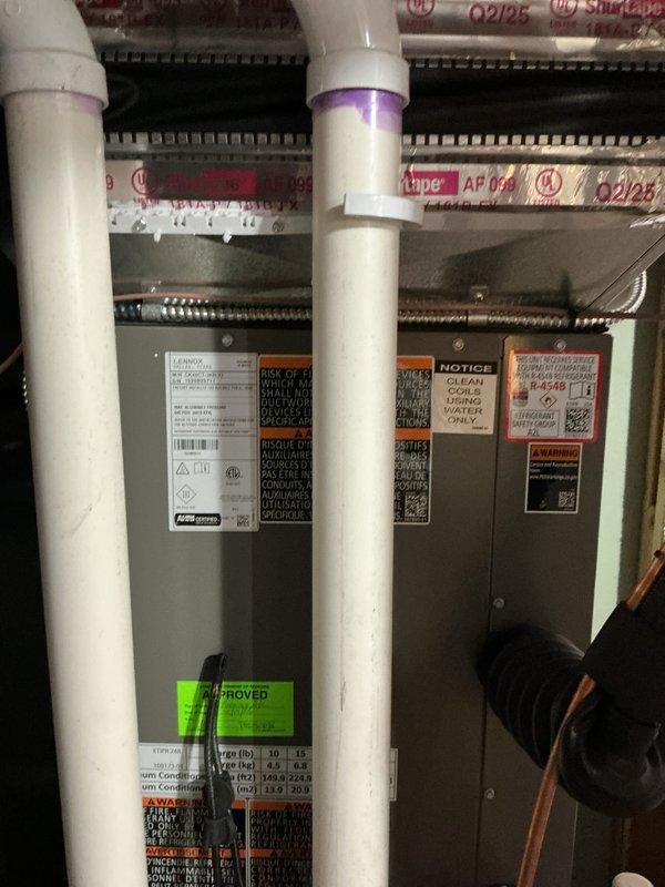 Completed system start-up and commissioning of dual air handling unit installation in basement mechanical room. Verified proper operation of both units, inspected refrigerant line connections, confirmed condensate drain lines are properly installed with appropriate PVC piping and primer application, and documented system condition with approval sticker placement indicating successful installation inspection.