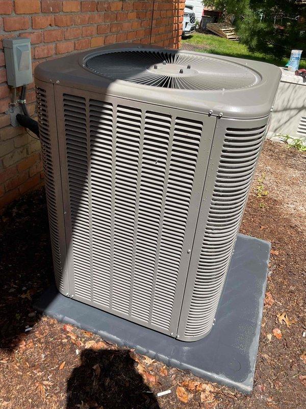 Performed comprehensive cooling system inspection on a 2-year-old residential air conditioning unit as part of annual maintenance plan renewal. Outdoor condenser unit located on concrete pad adjacent to building showed significant accumulation of dirt, dust, and debris in condenser coil fins. Conducted thorough visual assessment of equipment including fan assembly, electrical connections, and overall system operation. Air handler/coil located in basement was included in inspection protocol. Unit confirmed operational at time of service with no immediate mechanical failures noted. Documented equipment condition through photographic evidence showing exterior casing, fan grille assembly, and condenser coil contamination levels. Condenser fins displayed substantial clogging requiring attention to maintain optimal heat transfer efficiency and system performance. Electrical disconnect box and conduit connections inspected and found secure. Concrete mounting pad stable with proper equipment p