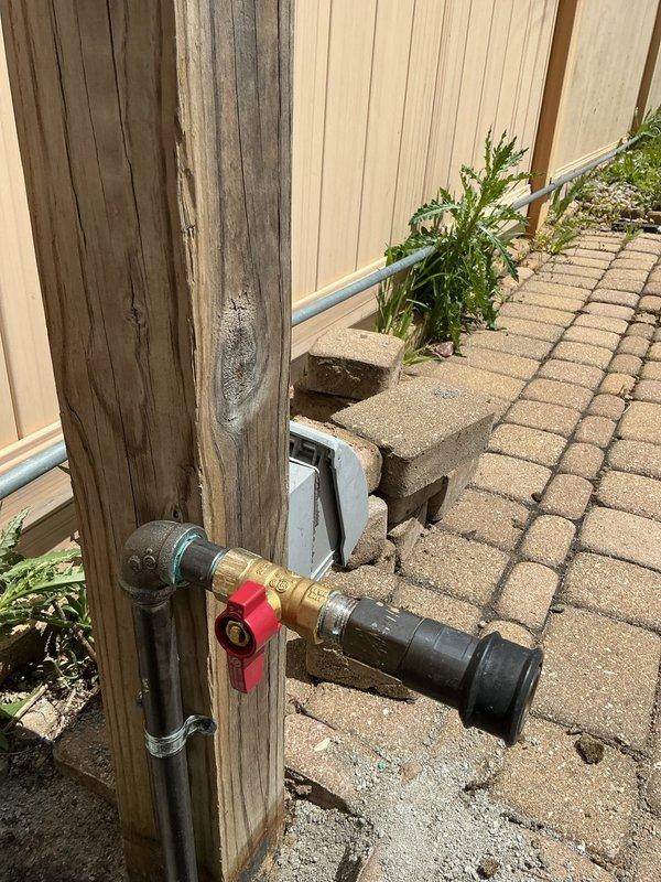 Responded to service call for reported gas leak beneath natural gas grill. Upon inspection, located corroded galvanized gas supply line in underground utility access area showing significant deterioration with visible perforations and rust damage along pipe exterior. Traced gas line from underground chamber to above-ground connection point at wooden post where shutoff valve and brass fittings were installed. Performed pressure test on gas system to verify leak location and assess system integrity. Documented extensive corrosion on underground pipe section requiring replacement to ensure safe operation. Shut off gas supply at valve with red handle to secure system until repairs could be completed. Recommended immediate replacement of compromised underground gas line section due to safety concerns from multiple perforation points and advanced pipe deterioration.