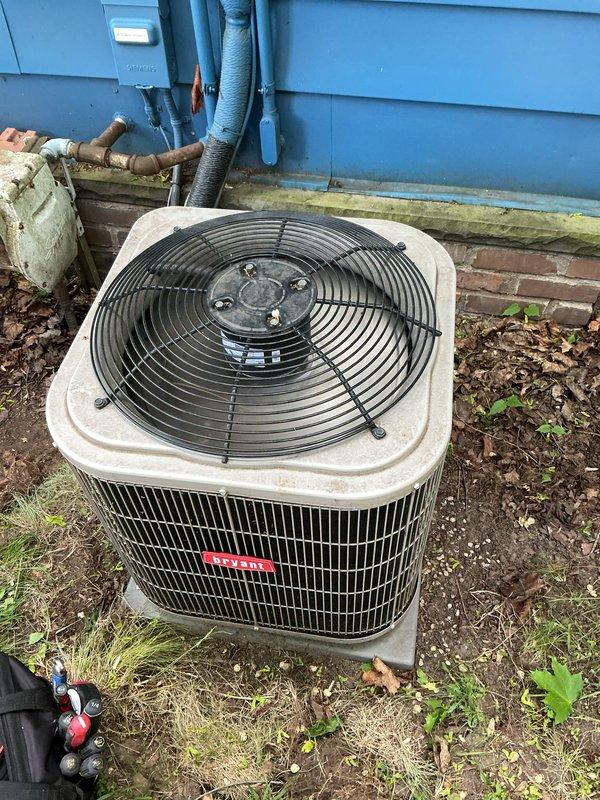 Completed comprehensive Gold AC Inspection on a 4-year-old residential split system with two units and air handler located in basement. Performed full system evaluation of outdoor condenser unit including visual inspection of cabinet condition, refrigerant line insulation, electrical disconnect, and fan grille assembly. Noted debris accumulation on top grille and surrounding area with vegetation growth near unit base. Verified equipment operational status, documented system configuration, and captured photographic records of exterior condenser placement and condition. Recommended routine debris removal from top grille to maintain optimal airflow and system efficiency.