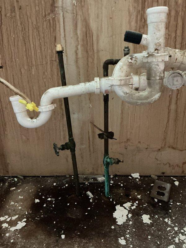 Provided estimate for complete removal of existing boiler piping system and capping of incoming water supply line to decommissioned boiler. Assessed extensive network of aged copper piping throughout basement mechanical room showing significant corrosion, green patina buildup, and oxidation on valve assemblies. Evaluated corroded red-orange valve components in upper section requiring removal. Inspected PVC drain configuration and black supply lines in utility area. Documented deteriorated plumbing infrastructure, water-damaged wooden surfaces, and accumulated debris. Estimate includes disconnection and removal of all copper pipes connected to boiler system, proper capping and securing of main water supply line to prevent future water flow to unit, and disposal of removed materials.