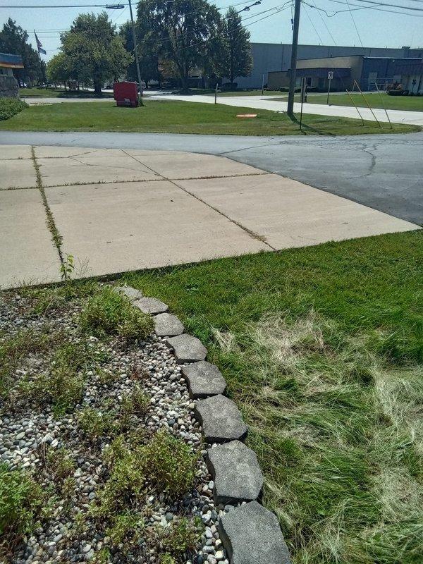 Responded to commercial property request to inspect exterior drainage system and evaluate potential sump pump needs. Conducted thorough site assessment of outdoor drainage infrastructure, documenting conditions with photographic evidence. Observed significant water accumulation in unpaved alleyway with visible algae growth indicating prolonged standing water and inadequate drainage. Identified drainage grate in roadway center with pooling water and poor surface grading contributing to retention issues. Examined perimeter drainage along building exterior, noting gravel-filled drainage areas with decorative concrete borders and mixed vegetation growth. Assessment revealed maintenance concerns including overgrown grass, muddy surface conditions with visible tire tracks, and compromised drainage functionality. Documented algae-covered puddles suggesting chronic drainage problems requiring intervention. Evaluated overall site drainage capacity and identified areas requiring remediation to p