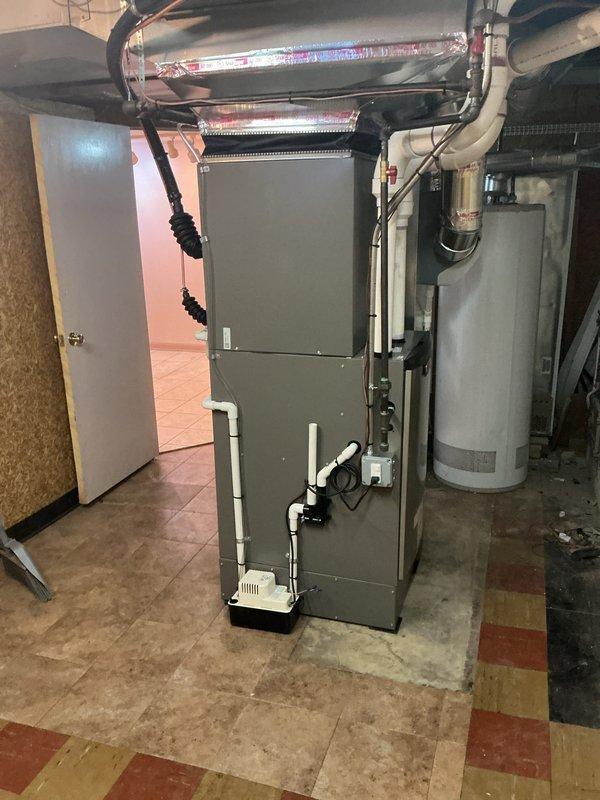 Completed installation of first-floor HVAC system including new furnace and air conditioning unit in basement utility room. Installed gray metal furnace on concrete pad with white PVC venting, flexible ductwork, condensate pump with drainage tubing, and proper electrical connections. System was permitted and qualifies for DTE energy rebate with AHRI certificate 216721606.