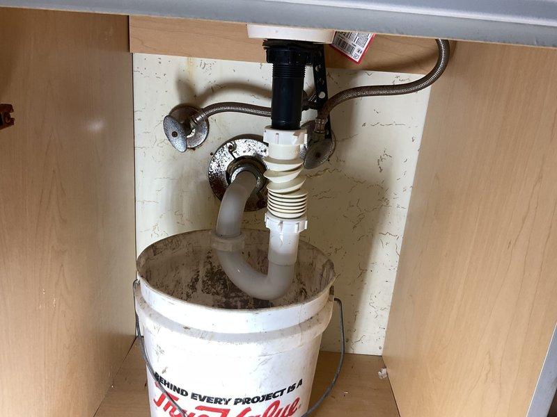Responded to commercial plumbing repair for kitchen faucet valve replacement. Upon arrival, identified failed valve cartridge in stainless steel kitchen sink faucet assembly. Disassembled faucet components, removed defective valve stem, and documented existing plumbing configuration including under-sink drainage system with P-trap and garbage disposal unit. Ordered Speakman RPG05-0534-CA replacement cartridge for installation. Placed bucket under sink to catch any residual drainage during service. Work area secured and customer notified of parts procurement timeline for completion of repair.