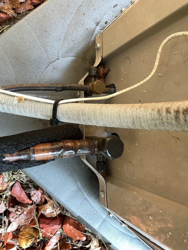 Completed scheduled maintenance inspection on 14-year-old air conditioning system with basement evaporator coil. Performed visual assessment of outdoor condenser unit, noting weathered housing with dirt accumulation and aged refrigerant lines showing significant corrosion on bare copper piping and staining on insulation wrap. System operational at time of inspection with fan assembly and protective grille intact.
