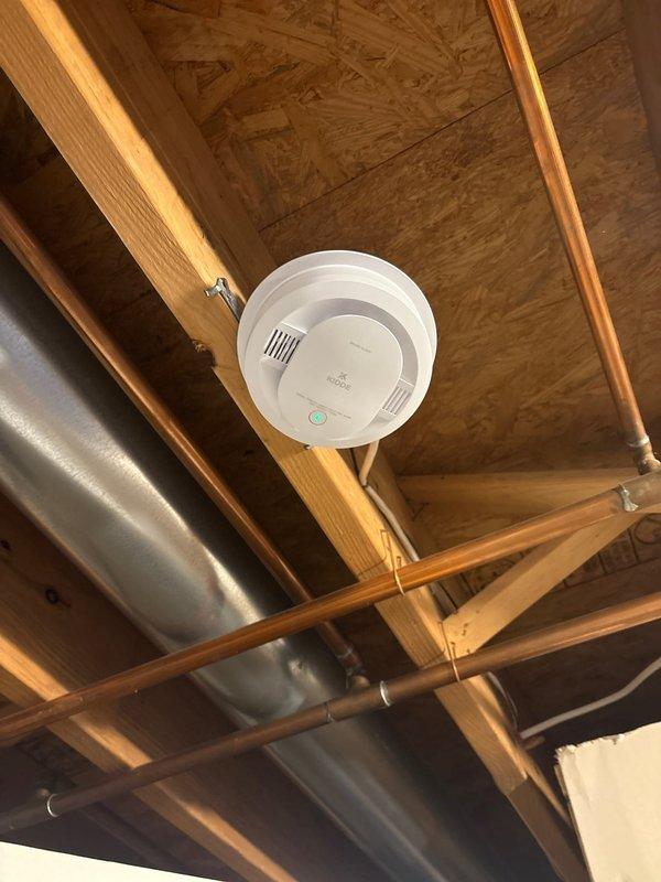 Removed existing smoke detector from ceiling and installed new replacement unit in attic space. Verified proper mounting to structural framework, tested functionality including LED indicator operation, and confirmed detector was securely fastened to ceiling surface per manufacturer specifications.