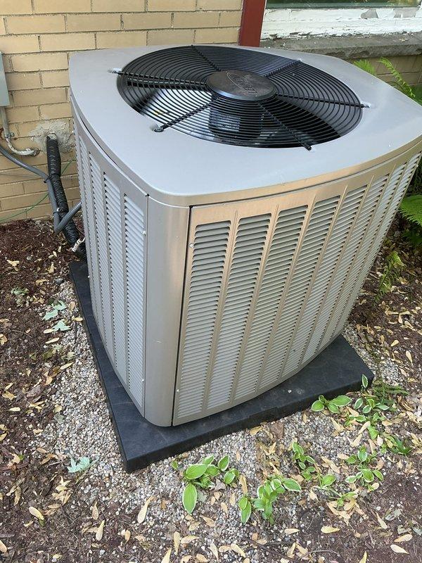 Completed comprehensive Gold AC inspection on 6-month-old residential air conditioning system with air handler located in basement. Performed thorough evaluation of outdoor condenser unit, which was found in excellent operational condition with proper installation on rubber pad and adequate clearance from building structure. Verified unit is functioning correctly with no mechanical issues, refrigerant lines properly secured, electrical connections intact, and condenser coils clean with appropriate airflow through louvered panels. Confirmed fan guard in place and protective measures adequate. Surrounding area showed minimal debris accumulation with some vegetation growth near base, which poses no immediate operational concerns. System passed all inspection criteria and is operating within normal parameters for equipment of this age.