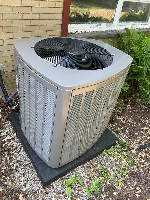 Completed comprehensive Gold AC inspection on 6-month-old residential air conditioning system with air handler located in basement. Performed thorough evaluation of outdoor condenser unit, which was found in excellent operational condition with proper installation on rubber pad and adequate clearance from building structure. Verified unit is functioning correctly with no mechanical issues, refrigerant lines properly secured, electrical connections intact, and condenser coils clean with appropriate airflow through louvered panels. Confirmed fan guard in place and protective measures adequate. Surrounding area showed minimal debris accumulation with some vegetation growth near base, which poses no immediate operational concerns. System passed all inspection criteria and is operating within normal parameters for equipment of this age.
