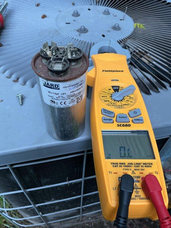 Responded to service call for non-operational 8-year-old outdoor AC unit. Upon arrival, performed diagnostic testing using digital multimeter to assess electrical components. Testing revealed failed capacitor, as indicated by open-loop reading on meter. Removed defective JARD capacitor from unit and prepared system for replacement. Documented equipment condition with photos showing capacitor failure and overall unit status. Unit exterior showed normal wear for age with debris accumulation on top grille and surrounding landscape area. Condenser coils and fan assembly inspected during diagnostic process.