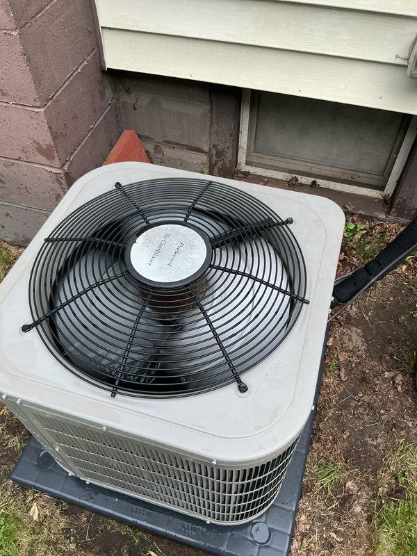 Completed Gold AC Inspection on a 7-year-old single air conditioning system with air handler located in basement. Verified equipment operational status with homeowner present. Performed comprehensive visual inspection of outdoor condenser unit, confirming proper installation on composite pad with adequate clearance from foundation. Inspected exterior electrical disconnect box mounted on vinyl siding, verified weatherproof cover functionality and conduit connections. Documented equipment condition through photographic records showing condenser unit positioning, fan guard integrity, and electrical components. All systems confirmed operational at time of inspection.