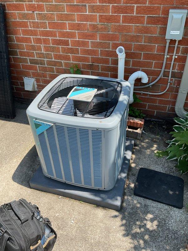 Completed comprehensive Gold AC inspection on 10-year-old residential air conditioning system with air handler and coil located in basement. System confirmed operational with all components functioning properly. Inspected outdoor condensing unit positioned on concrete pad against building exterior, verified proper clearances and mounting on rubber isolation pad, and checked electrical disconnect box and conduit connections. Examined indoor air handler assembly including drain pan with secondary overflow protection, verified proper drain line installation and connections, and confirmed all safety labels and installation notices present. Advised customer to maintain clear area around outdoor condenser unit, removing any debris or animal waste to ensure proper airflow and system efficiency.