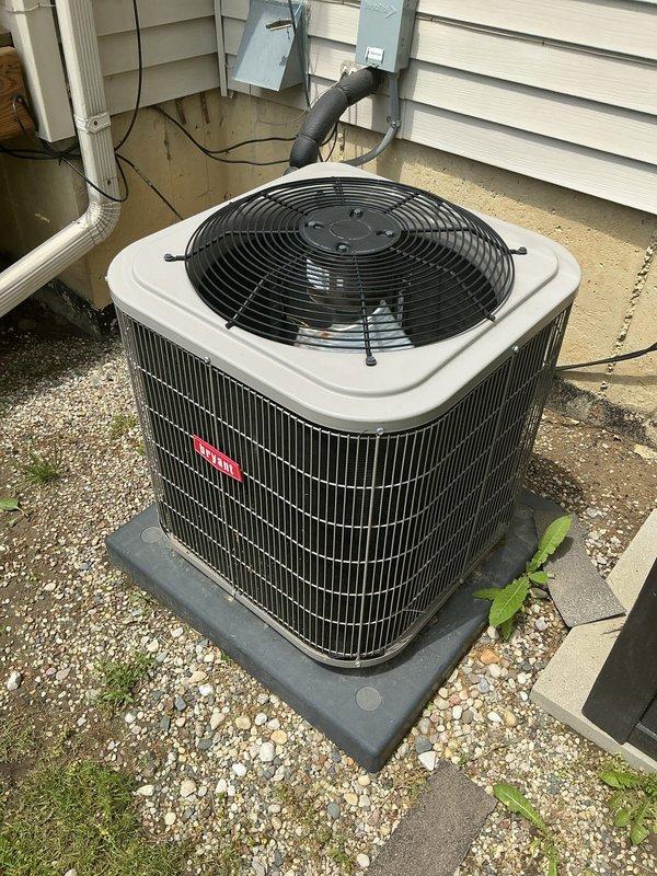 Completed comprehensive NSP AC inspection on a 5-year-old single-unit residential air conditioning system with air handler located in basement. Performed visual inspection of outdoor condensing unit installed on composite pad against exterior wall, verified proper installation with electrical disconnect box and refrigerant lines in place. Unit operational at time of inspection with no immediate service concerns identified. Documented equipment condition with photographs showing condenser on gravel base with adequate clearance, though minor vegetation growth noted around unit perimeter that may require periodic maintenance for optimal airflow.