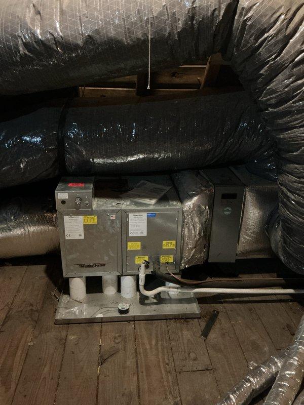 Assessed non-functional 14-year-old Unico HVAC system located in attic space for replacement estimate. Inspected existing air handler unit and associated ductwork configuration, including multiple flexible ducts and cylindrical supply lines measuring 12 and 14 inches in diameter. Documented equipment location, confirmed adequate attic access and working space, and verified air conditioning supply to attic area for comfortable working conditions during future installation.