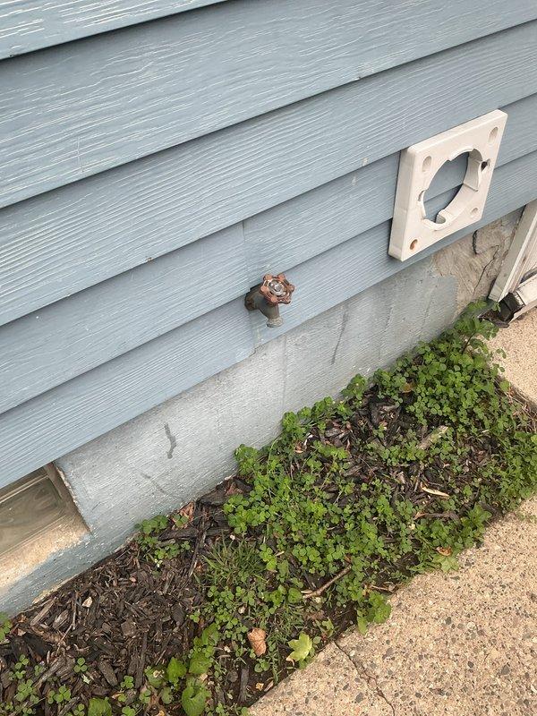 Responded to service call for installation of vacuum breaker on sump pump discharge line to meet municipal code requirements. Upon arrival, located exterior sump pump discharge point on building's exterior wall with light blue vinyl siding. Existing discharge configuration consisted of copper pipe penetration through foundation with basic hose bib valve assembly.

Installed atmospheric vacuum breaker assembly on the discharge line to prevent potential backflow contamination of potable water supply. The vacuum breaker was mounted on tan square backing plate secured to exterior wall above the existing valve assembly. This device provides required air gap protection by allowing air to enter the system when pressure drops, preventing siphonage back into the building's water supply system.

Verified proper installation orientation with vacuum breaker positioned vertically and installed downstream of any shutoff valves per plumbing code standards. Tested valve operation and confirmed vacuum 