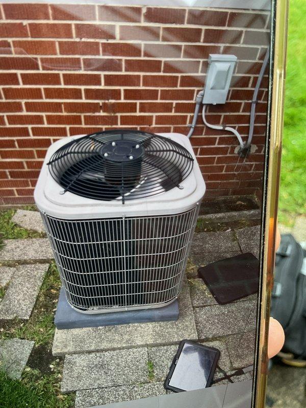 Completed comprehensive Gold AC inspection on 9-year-old residential air conditioning system with air handler located in basement and condensing unit positioned on exterior concrete pad. Performed multi-point inspection including verification of operational status, visual examination of outdoor condenser unit with proper clearance from debris, assessment of electrical disconnect and conduit connections at exterior wall mounting, and inspection of mechanical room equipment. System found operating properly with condenser coils clean, adequate airflow through top-mounted fan assembly, and all components functioning within normal parameters.
