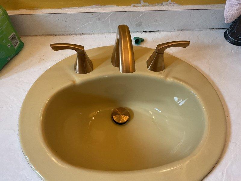 Completed installation of a new three-piece widespread bathroom faucet in brushed gold/bronze finish with matching drain assembly. Also installed an exterior hose bib with proper shutoff valve. All supply lines were connected with braided stainless steel hoses, P-trap was properly assembled with compression fittings, and all connections were tested for leaks to ensure proper operation.