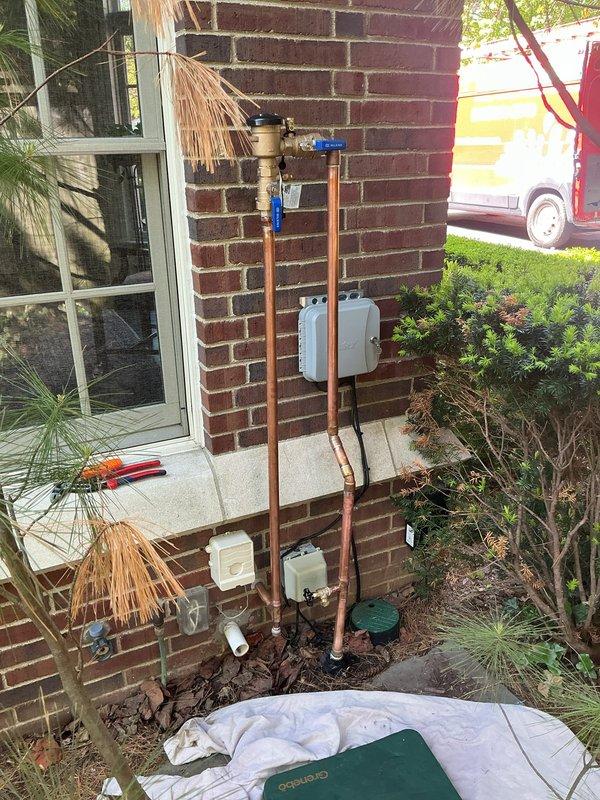Installed new PVB (Pressure Vacuum Breaker) backflow prevention device on exterior copper water line. The assembly includes a Wilkins brand backflow preventer with blue shut-off valve, properly mounted to brick exterior wall with appropriate support and clearance for testing and maintenance.