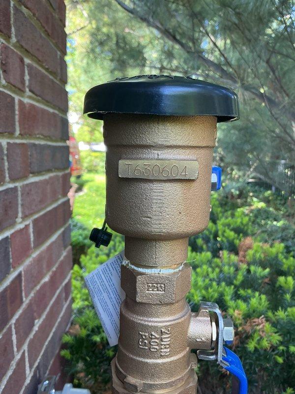 Installed new PVB (Pressure Vacuum Breaker) backflow prevention device on exterior copper water line. The assembly includes a Wilkins brand backflow preventer with blue shut-off valve, properly mounted to brick exterior wall with appropriate support and clearance for testing and maintenance.