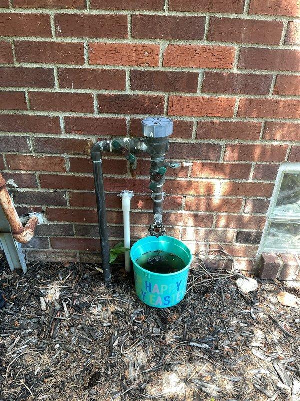 Conducted on-site assessment of existing backflow prevention assembly mounted on exterior brick wall for replacement quote. Documented current installation configuration including black iron pipe connections, shut-off valves, and drainage setup with collection bucket. Evaluated accessibility, existing pipe conditions, and mounting requirements for backflow preventer replacement to ensure compliance with local plumbing codes and cross-connection control standards.