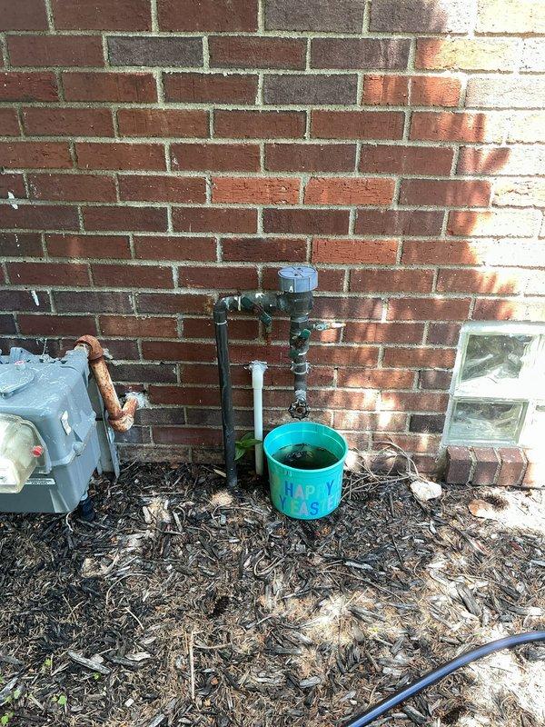 Conducted on-site assessment of existing backflow prevention assembly mounted on exterior brick wall for replacement quote. Documented current installation configuration including black iron pipe connections, shut-off valves, and drainage setup with collection bucket. Evaluated accessibility, existing pipe conditions, and mounting requirements for backflow preventer replacement to ensure compliance with local plumbing codes and cross-connection control standards.
