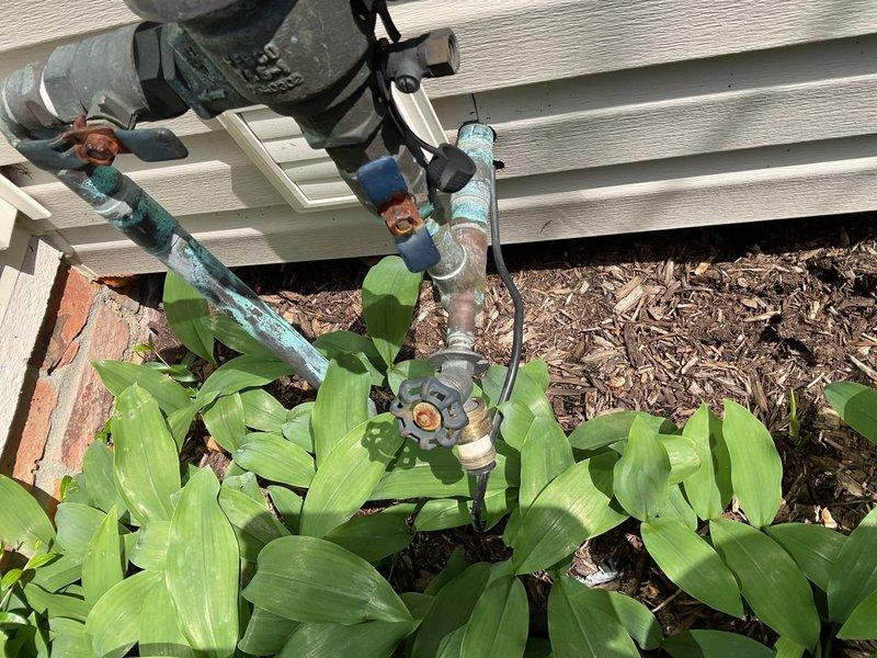 # Outdoor Spigot Replacement and Code Compliance Upgrade

Responded to service request for replacement of two exterior hose bibs requiring code compliance updates at front and rear yard locations. Upon arrival, assessed existing outdoor plumbing installations mounted on building exterior against brick and horizontal siding.

## Work Performed

**Front Yard Spigot Assembly:**
Removed existing weathered outdoor faucet system showing significant corrosion and aging. Existing configuration included deteriorated copper piping with blue-green patina buildup and heavily oxidized brass valve components with brown rust accumulation. Disconnected obsolete plumbing assembly including corroded galvanized fittings and compromised connection points. 

Installed new code-compliant frost-proof sillcock with proper pitch for drainage. Configured new copper supply line connections with lead-free solder joints. Integrated backflow prevention device per current plumbing code requirements. Secured all pipi
