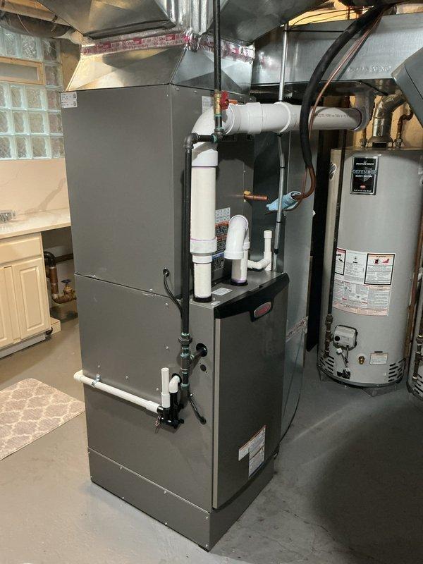 Completed full HVAC system installation including new furnace and air conditioning unit with outdoor condenser pad. Installed gray cabinet-style furnace in basement utility area with PVC venting and connected ductwork, positioned AC condenser on concrete pad in exterior side yard with proper electrical connections and refrigerant lines. Coordinated electrical work, obtained necessary permits, and submitted documentation for utility rebate program.