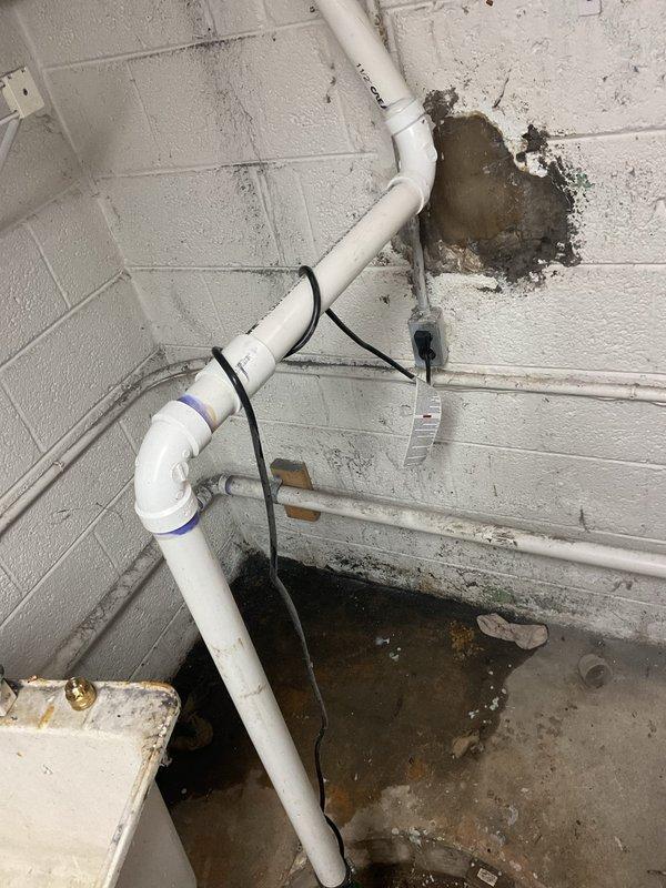 Completed plumbing repair in basement utility area addressing water intrusion and drainage issues. Repaired and secured white PVC piping system along concrete block walls, replacing damaged sections and properly fastening with mounting straps. Remediated standing water on concrete floor, identified source of leak at wall penetration point, and sealed damaged wall opening where pipe enters structure to prevent future water accumulation.