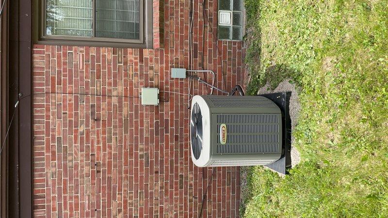 Completed installation of new air conditioning system and evaporator coil at residential property. Outdoor condenser unit positioned on concrete pad with rubber isolation pad against brick exterior wall, with electrical disconnect box mounted and conduit properly routed. System installation coordinated with permit requirements, though electrical work requires licensed electrician for final connections and service energization.