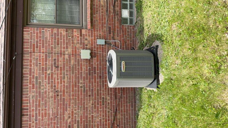 Completed installation of new air conditioning system and evaporator coil at residential property. Outdoor condenser unit positioned on concrete pad with rubber isolation pad against brick exterior wall, with electrical disconnect box mounted and conduit properly routed. System installation coordinated with permit requirements, though electrical work requires licensed electrician for final connections and service energization.